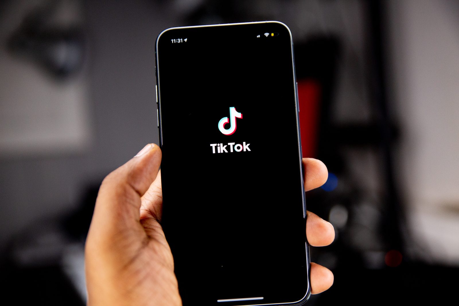 Kädessä puhelin, jossa auki TokTokin logo mustalla pohjalla.