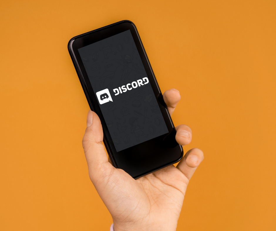 Musta puhelin on nostettu kädessä ilmaan oranssia taustaa vasten. Puhelimessa auki Discordin logo.