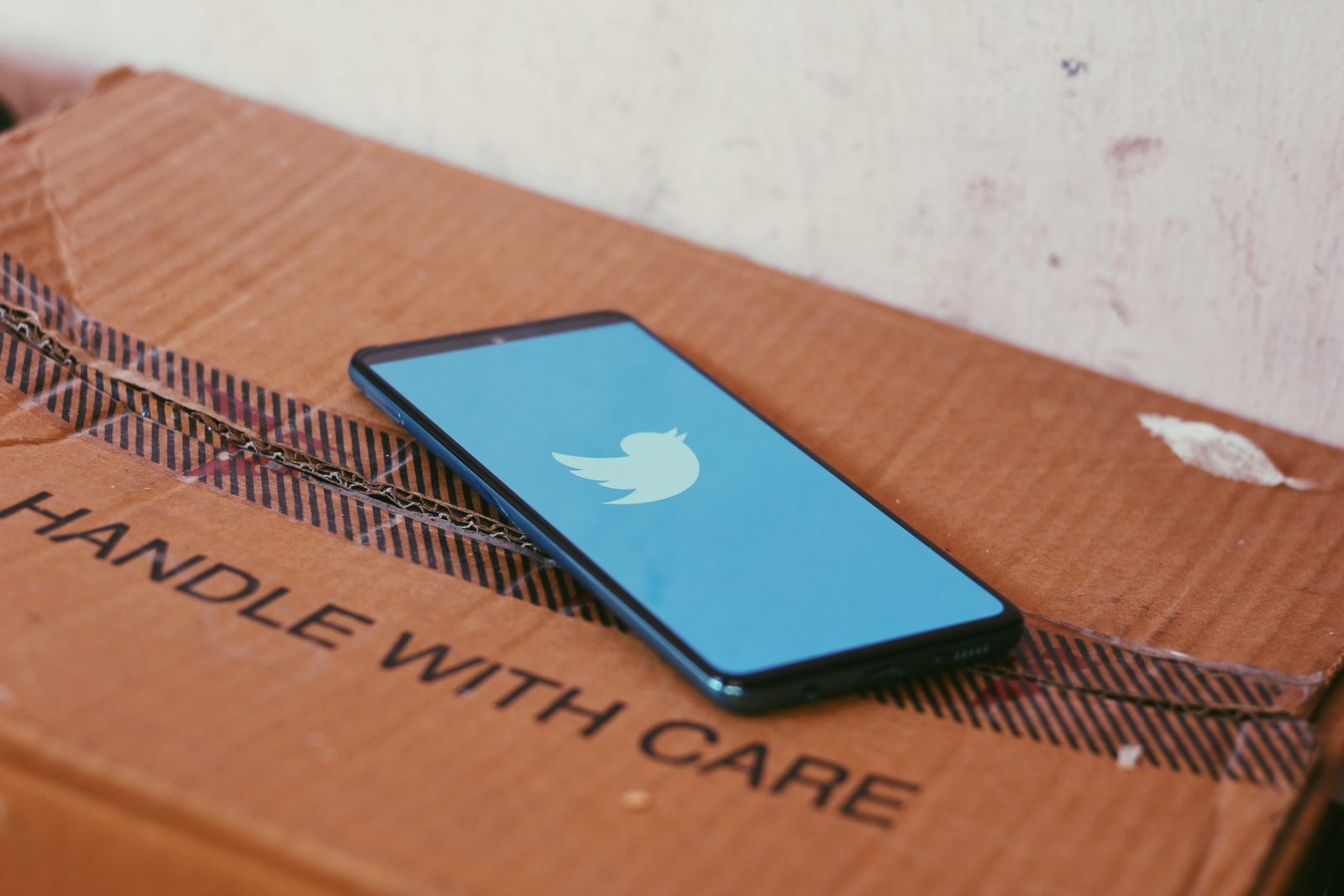 Pahvilaatikon päällä puhelin, jossa on auki Twitterin logo.