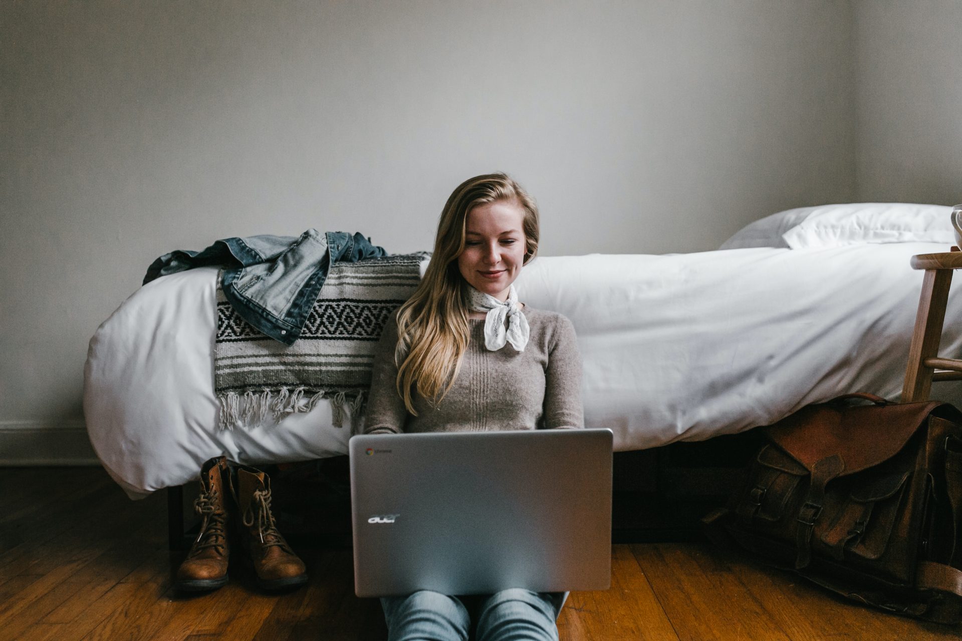 Woman sitting in front of the bed and watching her laptop.