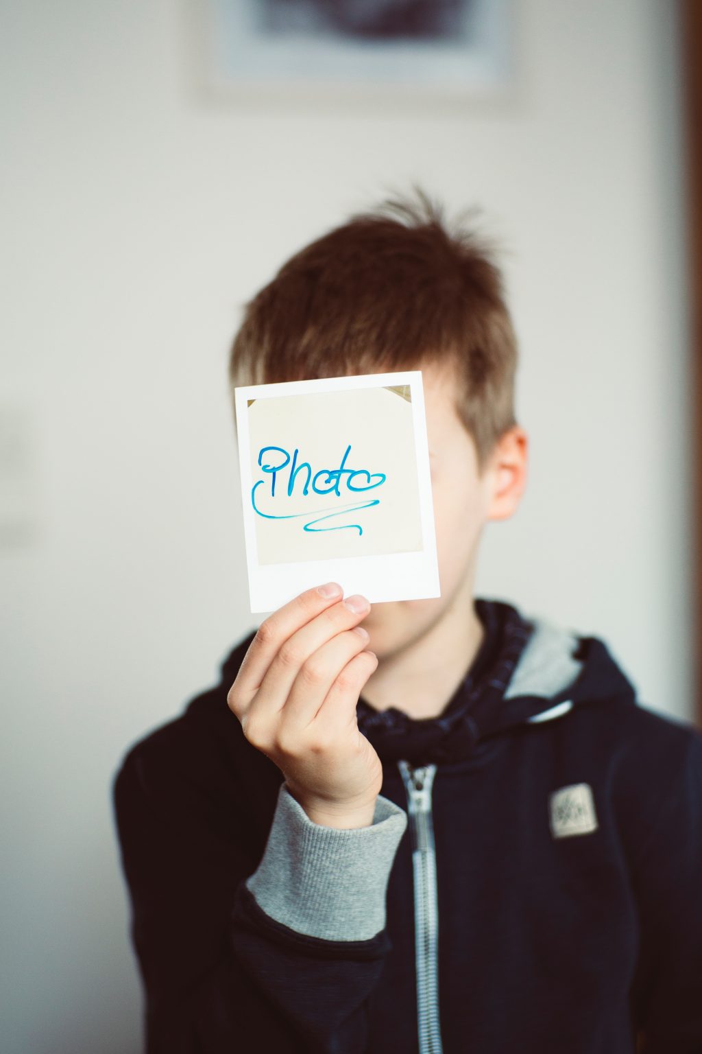Pieni poika pitää kasvojen edessä polaroid-kuvaa, jossa lukee photo.