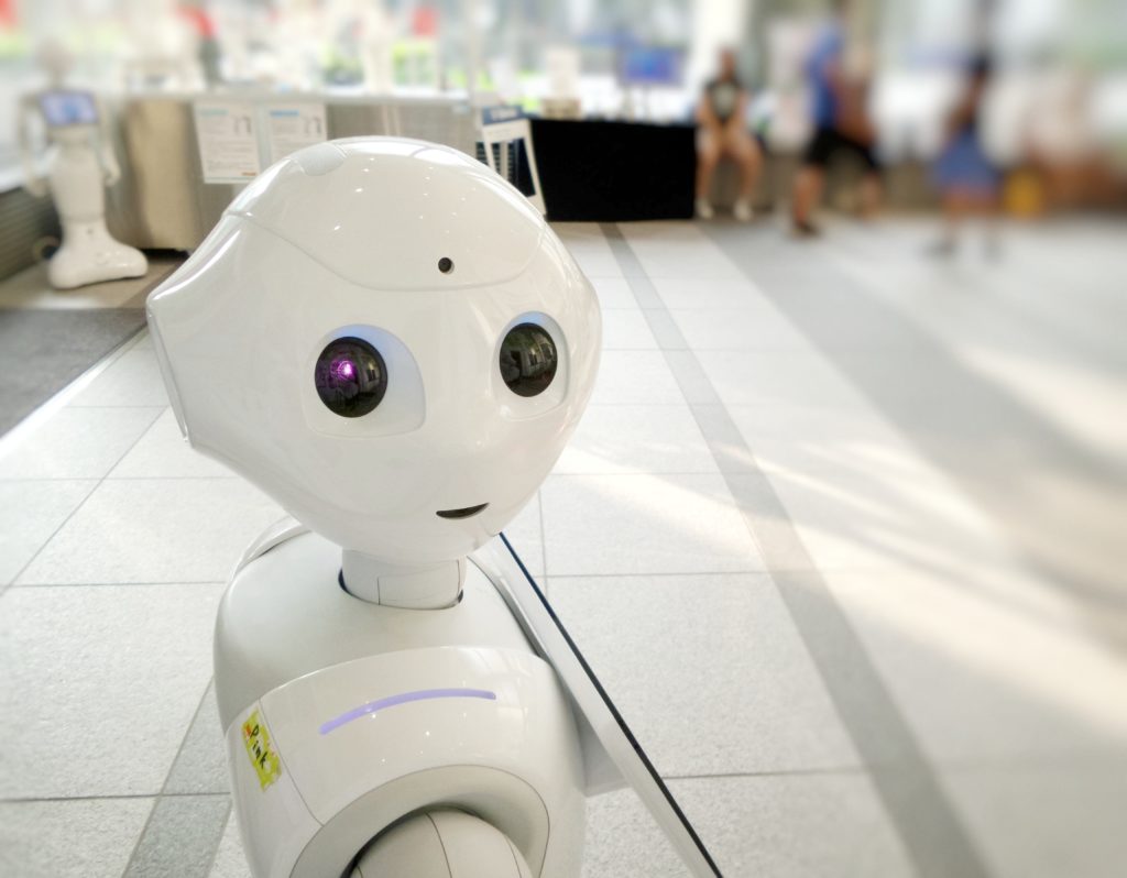 Valkoinen robotti katsoo kameran päin ja pitelee tablettia ostoskeskuksessa.