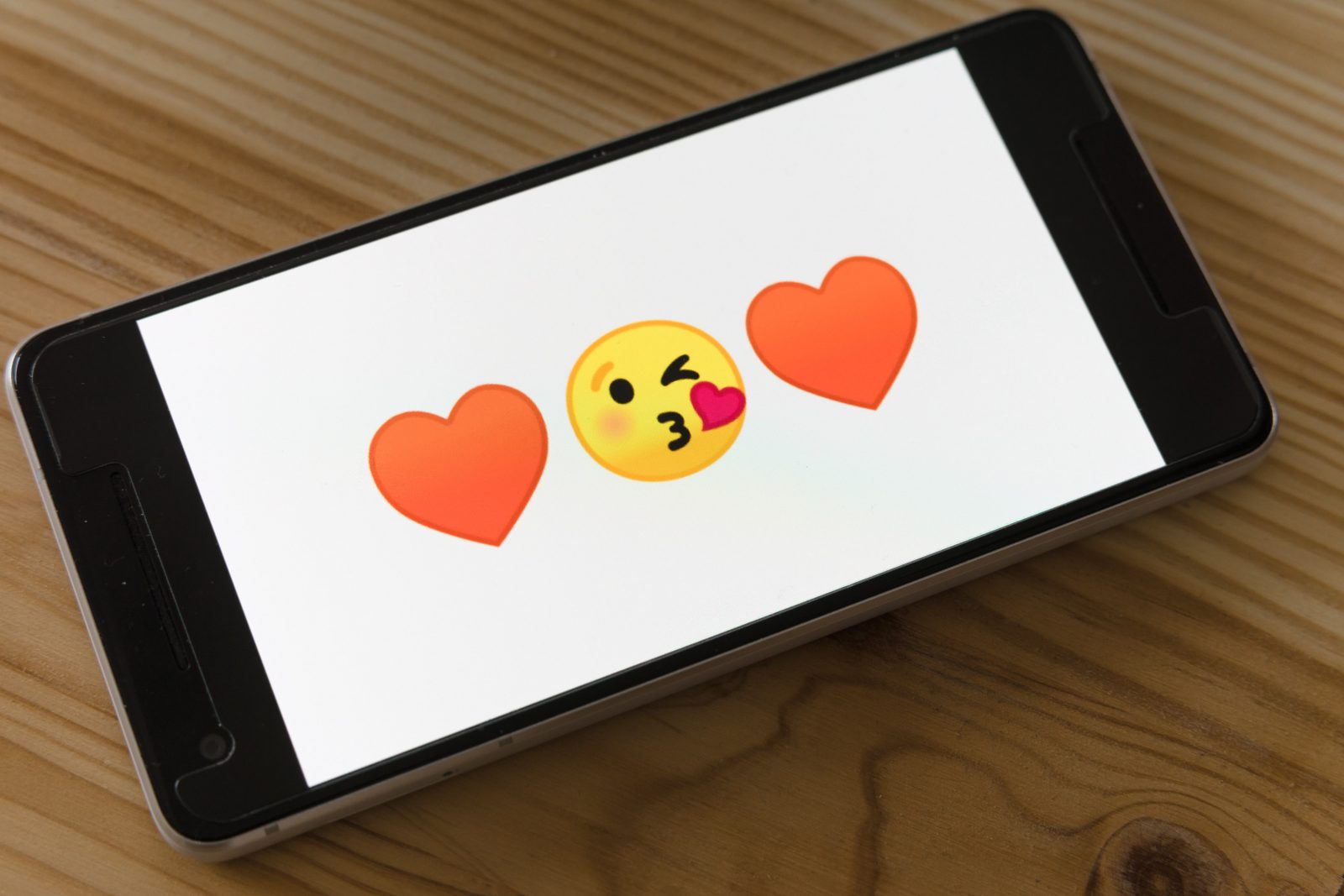 Puhelimen ruudulla kaksi sydän emojita, joiden välissä pusua antava emoji
