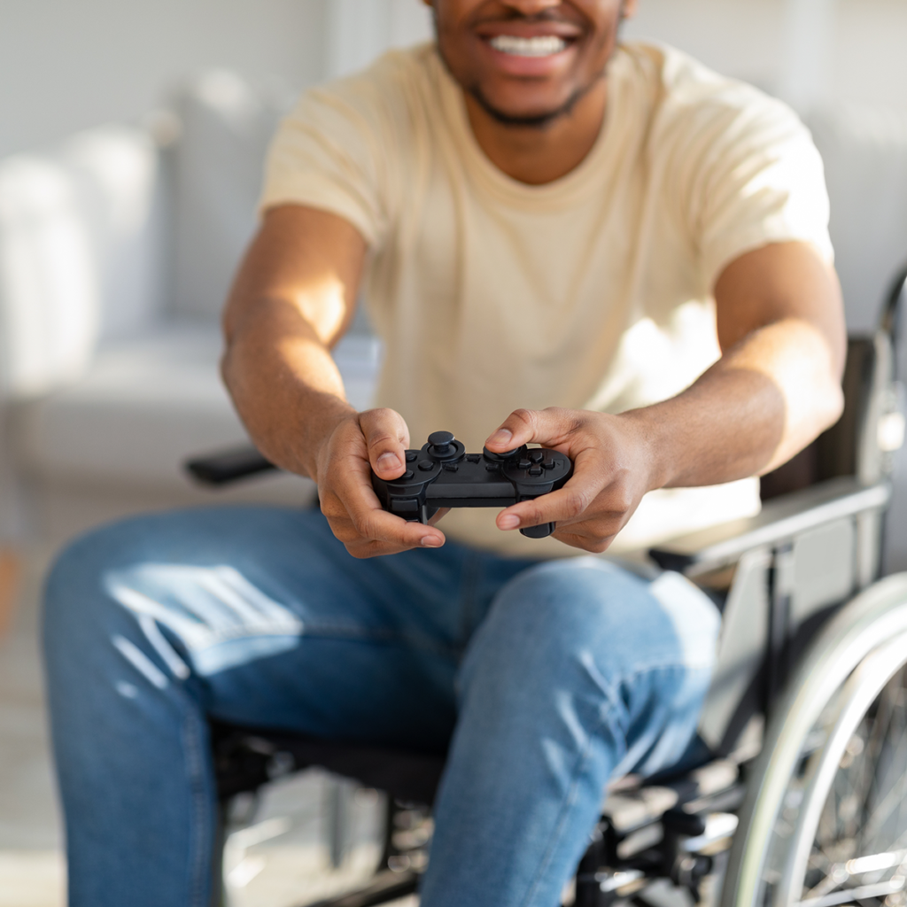 Tummaihoinen henkilö istuu pyörätuolissa ja pelaa konsolipeliä ohjaimella.