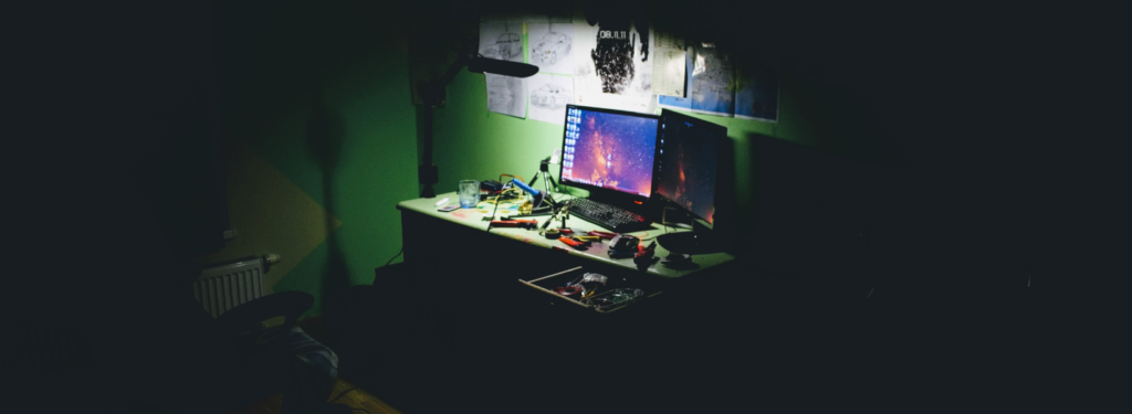 kuva tietokoneesta ja tavaroiden epittämästä pöydästä pimeässä huoneessa